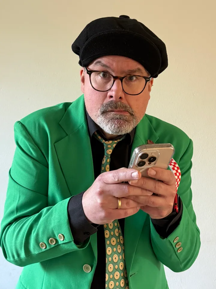 Sjefke in zijn groene colbert, met baret, kijkt verbaasd naar zijn telefoon